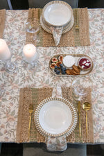 Elegant table setting with plates, glasses, and a small dish of food on a floral tablecloth.