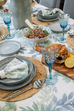 Dining table setting with plates, glasses, and food on a floral tablecloth.