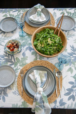 Dining table setting with green salad, blue plates, and floral tablecloth.