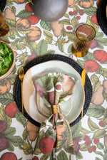 Dining table setting with a patterned tablecloth featuring fruits and vegetables, plates, and napkins.