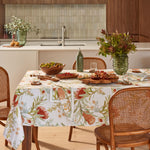 Native Harvest cotton floral tablecloth with orange flowers, green botanical foliage and earthy tones on a white background.