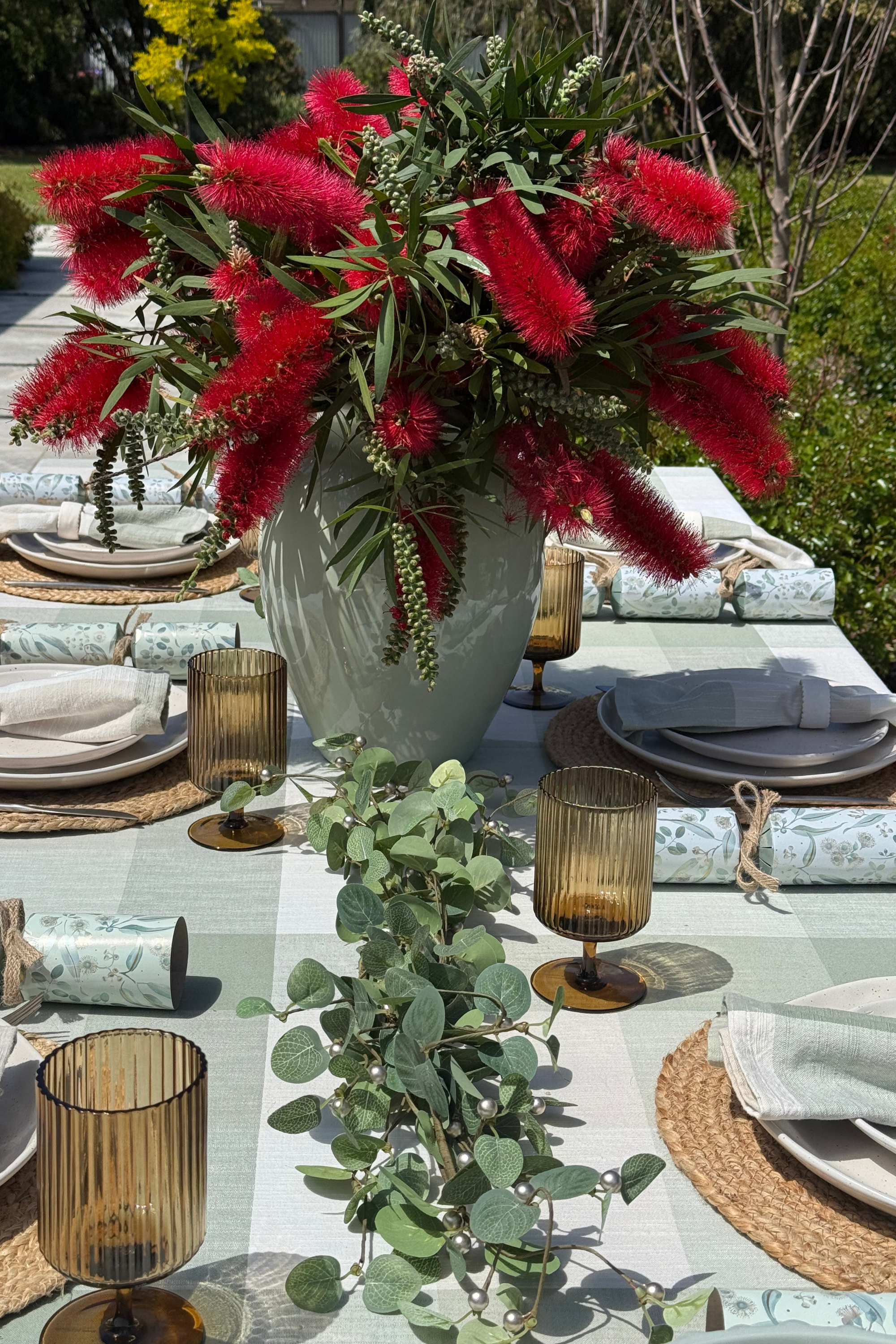 Elegant outdoor dining table setting with red floral arrangement and greenery.
