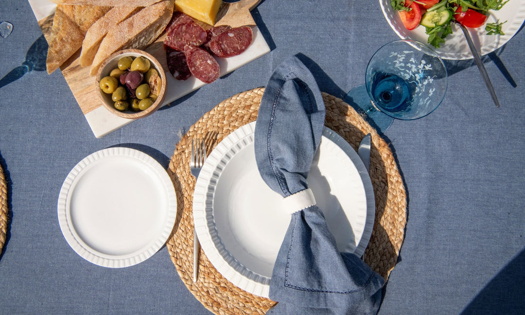 Dining table setting with plates, cutlery, and food on a blue tablecloth.