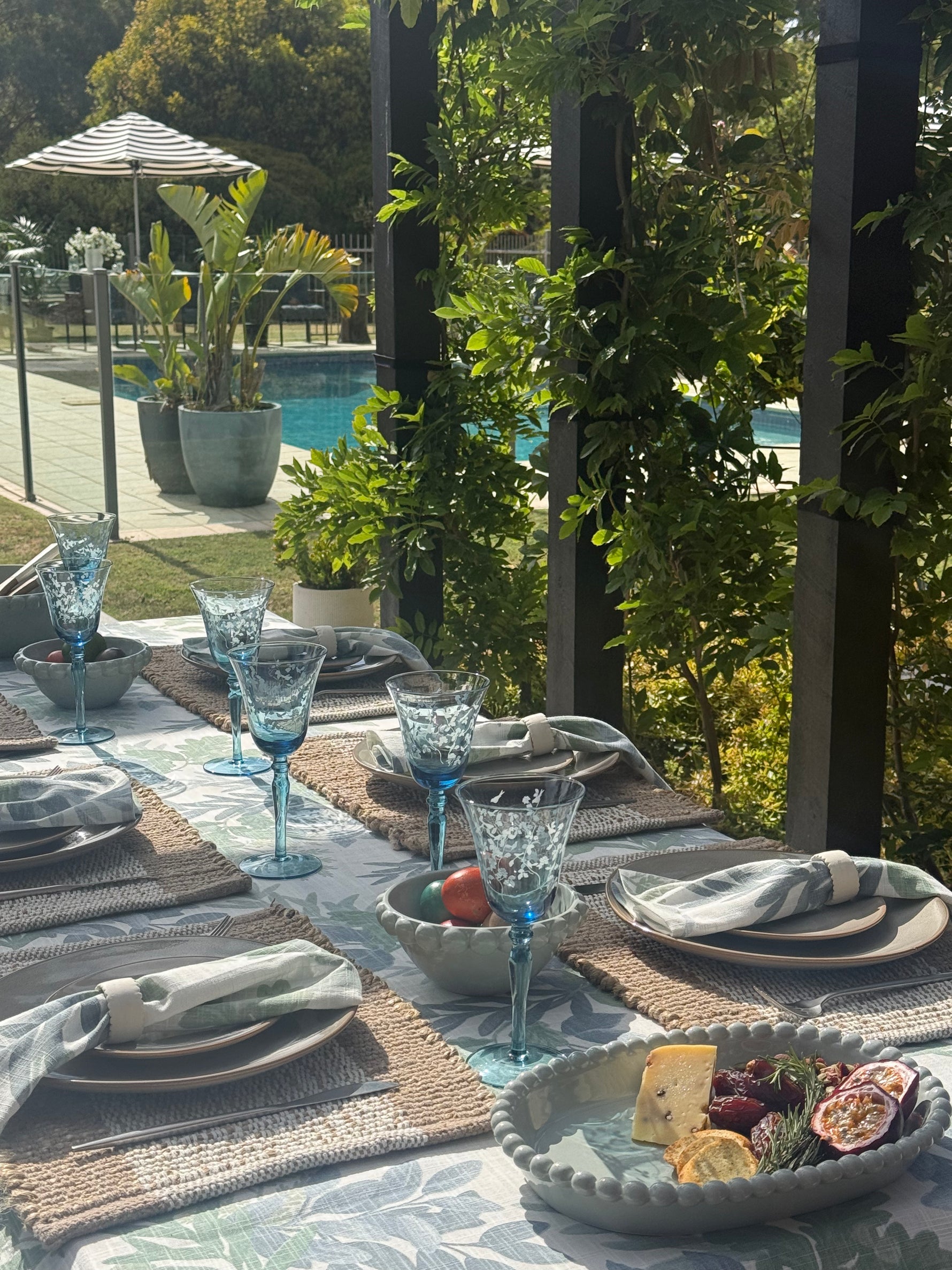 Outdoor dining table setting with blue glasses and appetizers by a poolside.