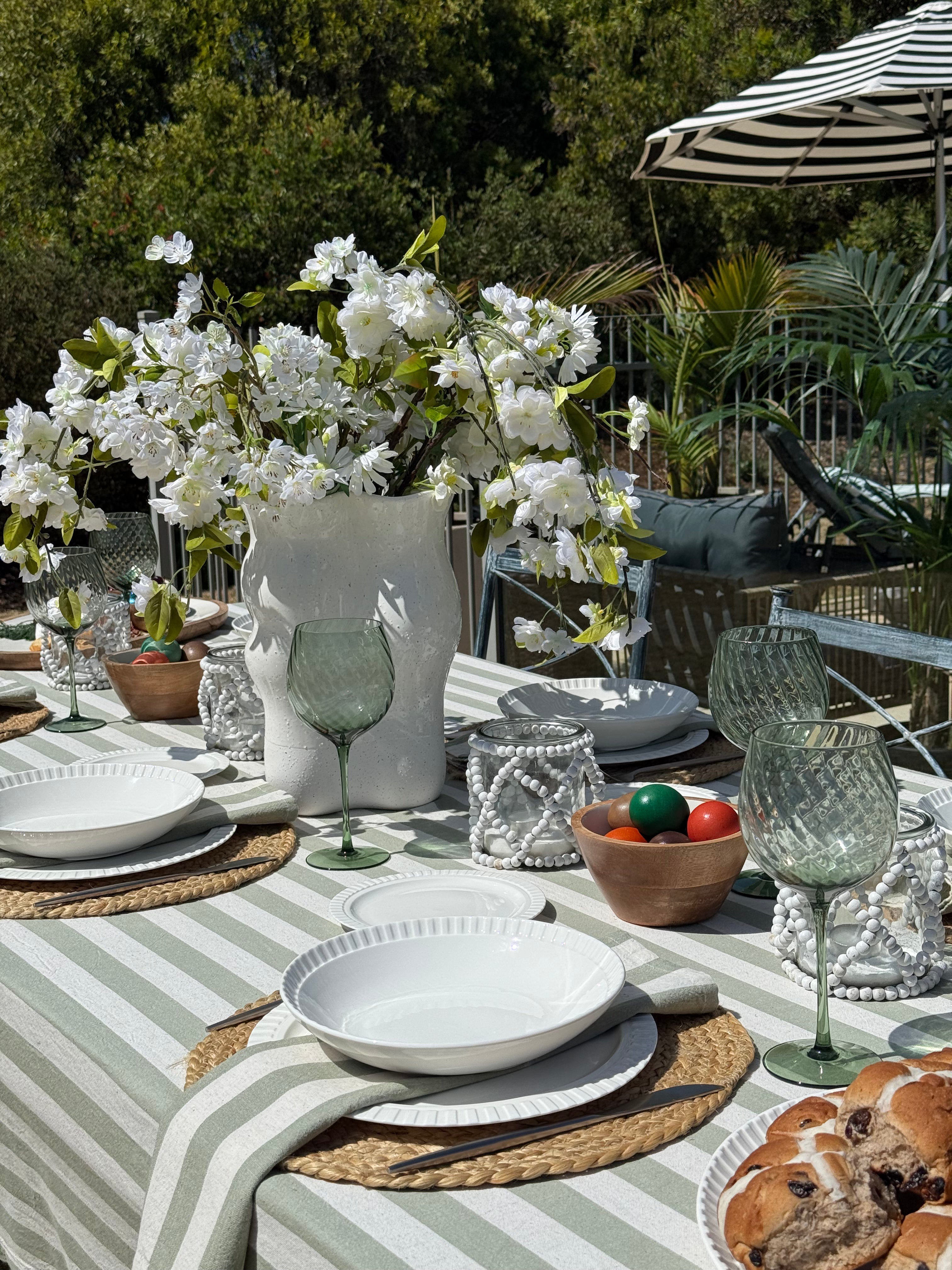 Outdoor dining table setting with white flowers, plates, glasses, and a striped tablecloth.