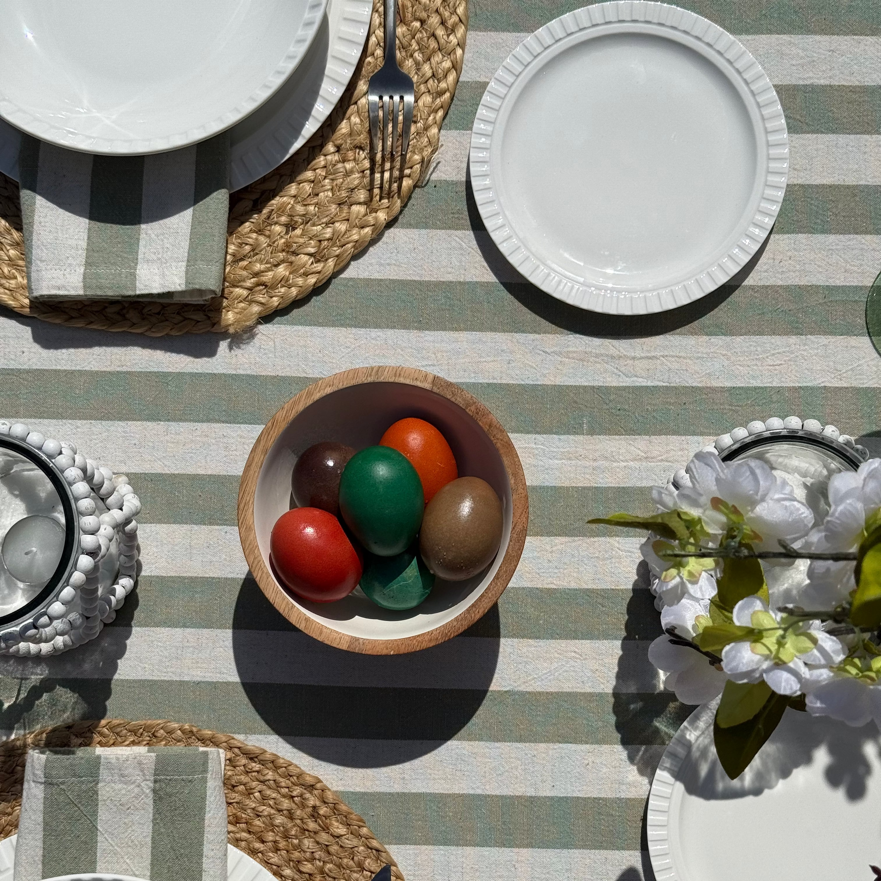 Table setting with white plates, a bowl of colorful eggs, and a striped tablecloth.