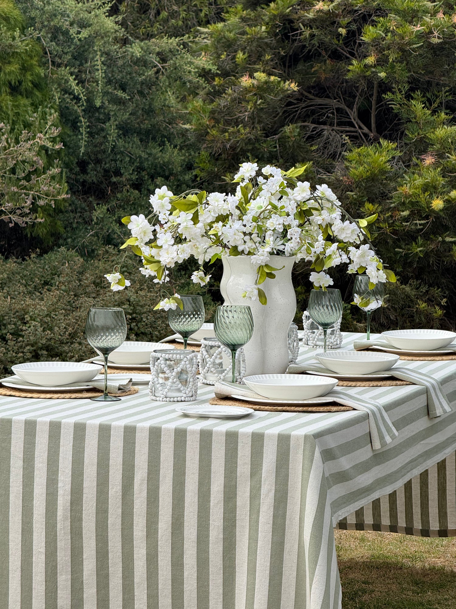 Olive Stone Stripe green and off-white cotton tablecloth with a classic striped pattern, styled on a rectangular dining table.