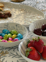 Bowls of colorful candies, cherries, and strawberries on a patterned tablecloth.